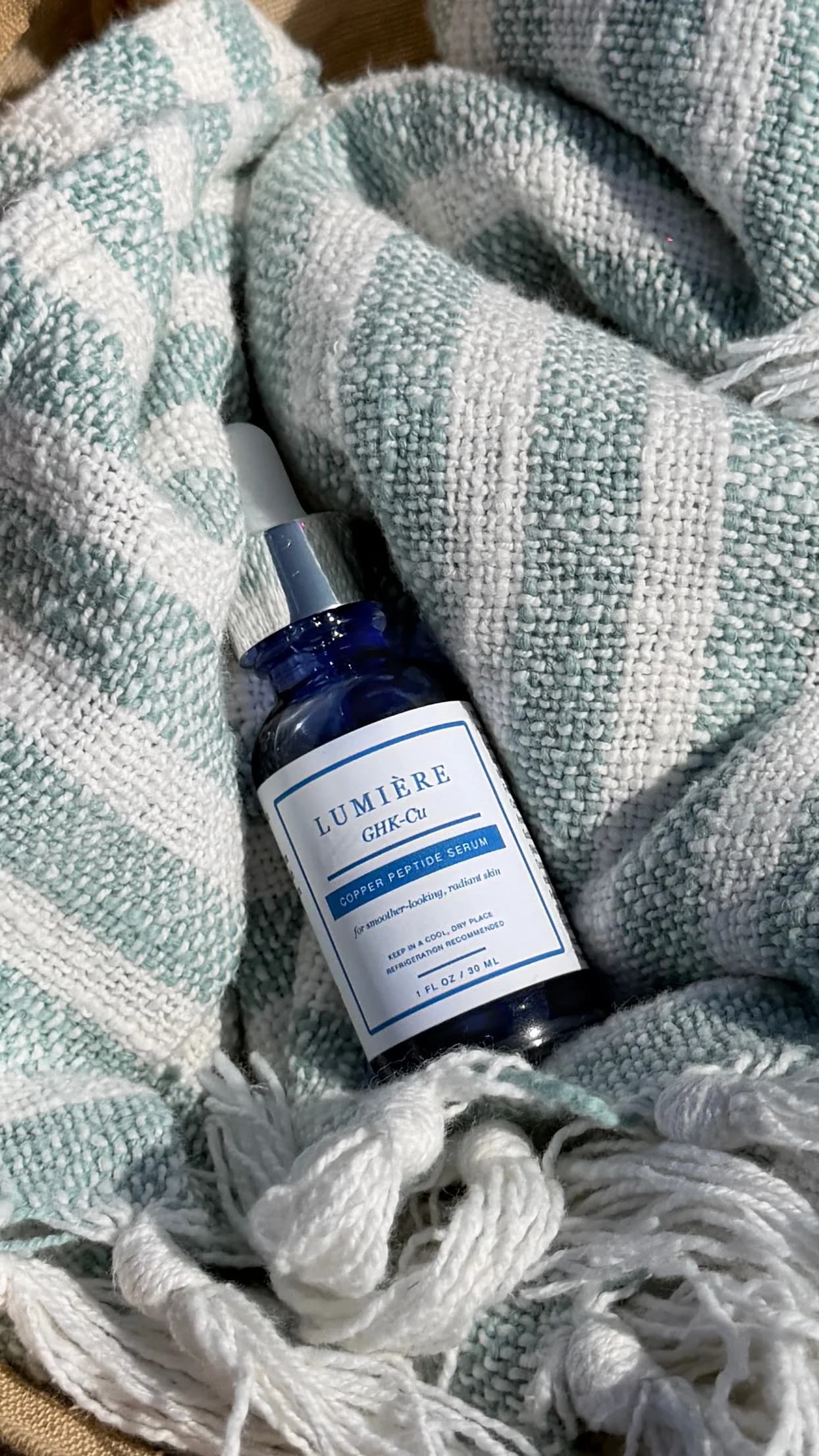 Lumiere serum nestled in the folds of a sea-green striped towel