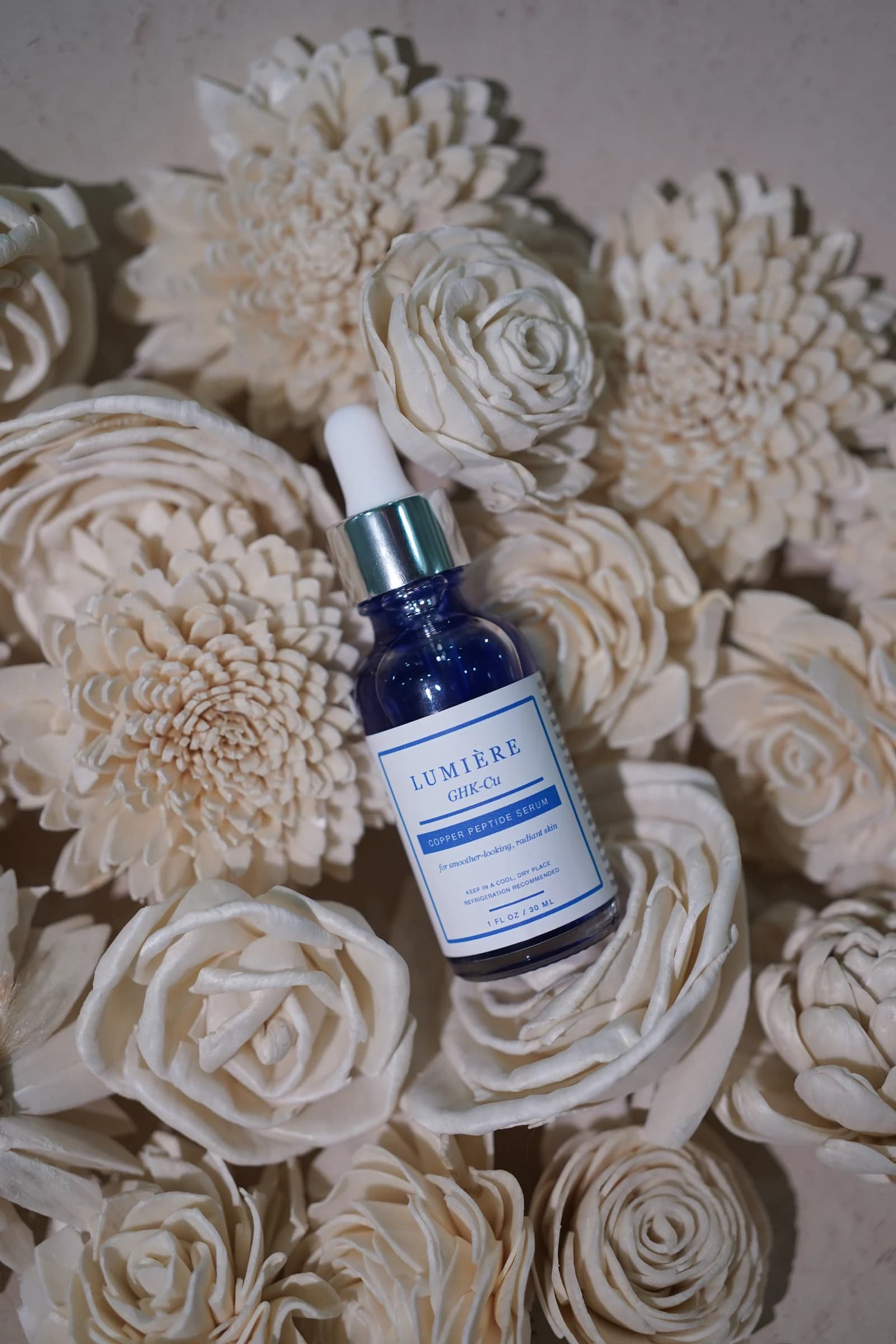The blue serum bottle arranged among cream-colored flowers