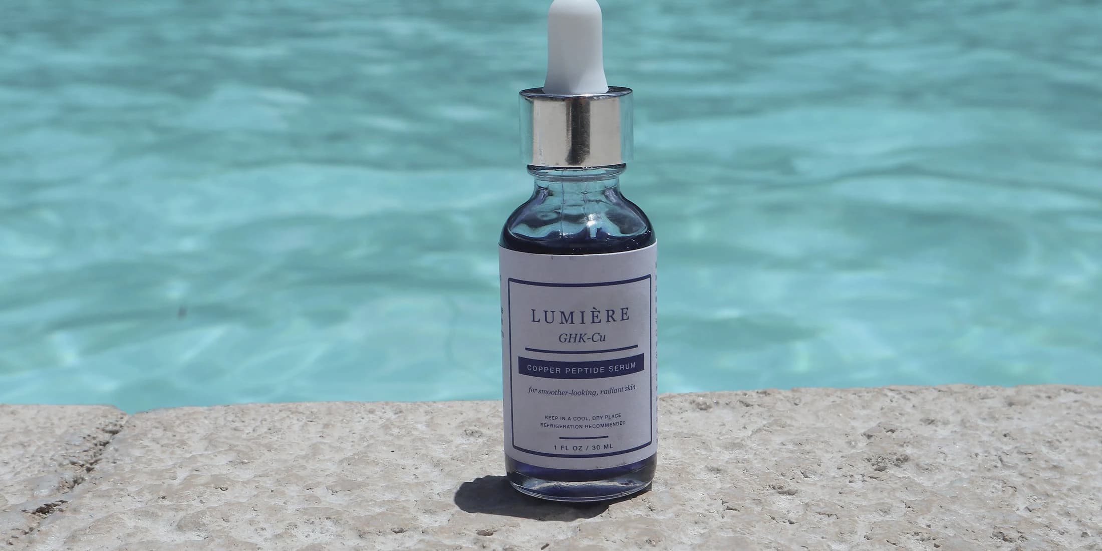 Lumiere Routine serum bottle beside turquoise pool water